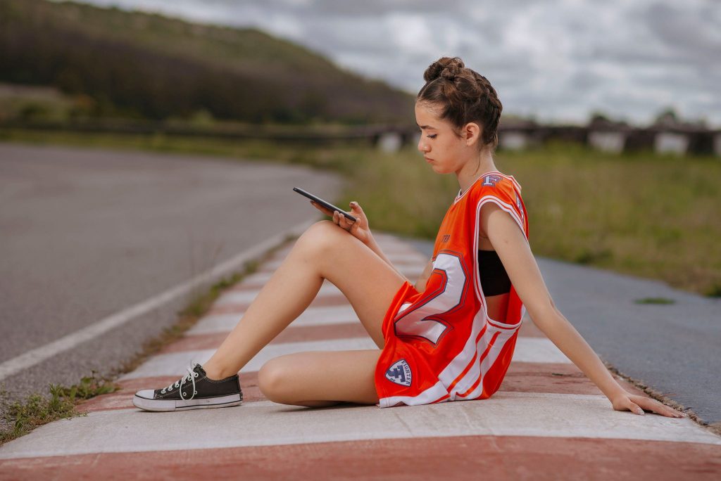 Estate senza scuola tra libertà e isolamento: ragazza seduta all’aperto mentre usa lo smartphone durante le vacanze estive.