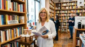 Mary Troiano in piedi all'interno di una libreria mentre sorride e tiene tra le mani una copia del suo libro durante una presentazione